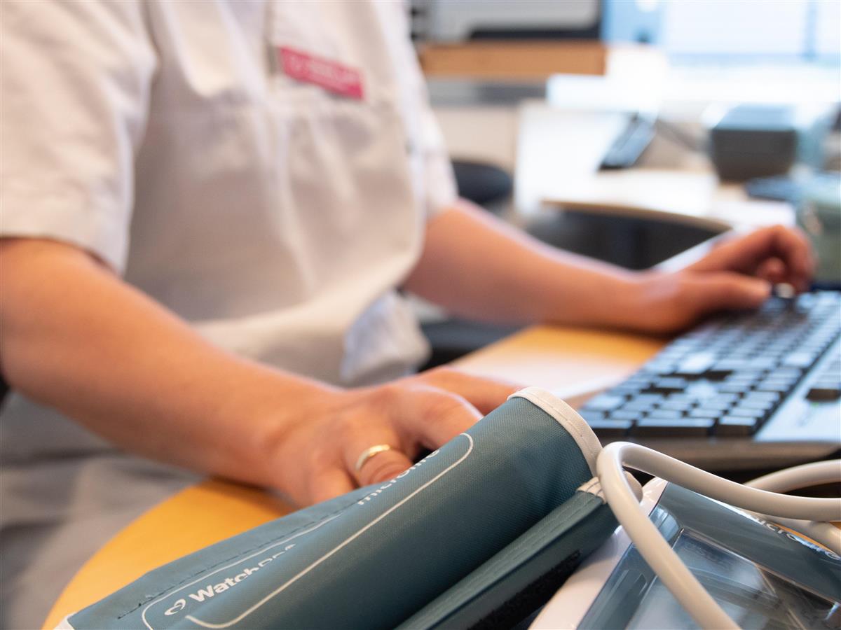 Ansatt i hvitt arbeidstøy sitter foran en PC og arbeider med nytt pasientjournalsystem. - Klikk for stort bilde