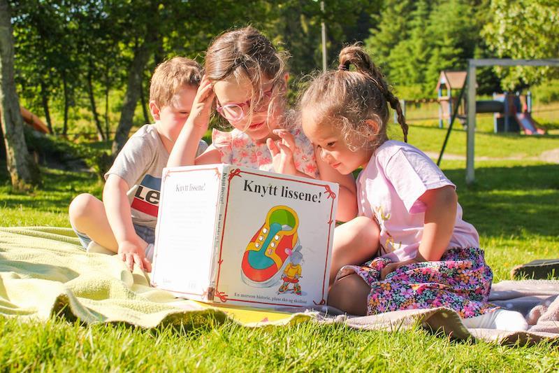 Bilde viser barn i et uteområdet som leser boka Knytt Lissene - Klikk for stort bilde